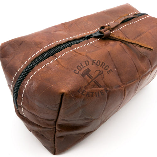 A brown leather zippered pouch with white contrast stitching and a black zipper, shown on a white background.