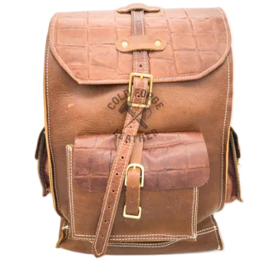 A brown leather backpack with crocodile-embossed and smooth panels, featuring brass-tone buckle closures and white contrast stitching, shown against a plain white background.