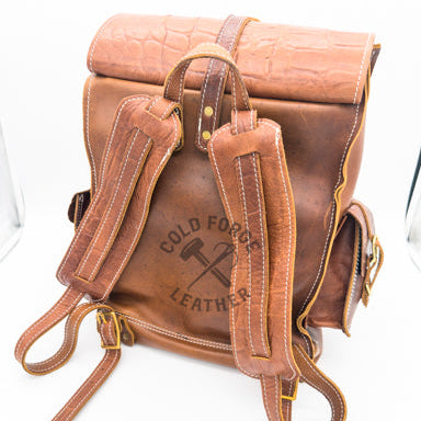A brown leather backpack with a crocodile-embossed top flap, adjustable padded shoulder straps, 