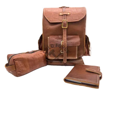 A brown leather backpack set displayed on a white studio background, including a main backpack with front flap and buckle closure, a matching cylindrical pouch, and a matching jourmal. 