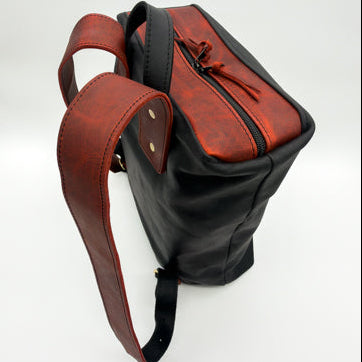 A handmade minimalist leather backpack with a split design featuring a black leather body and a reddish leather top panel and straps, shown on a white background.