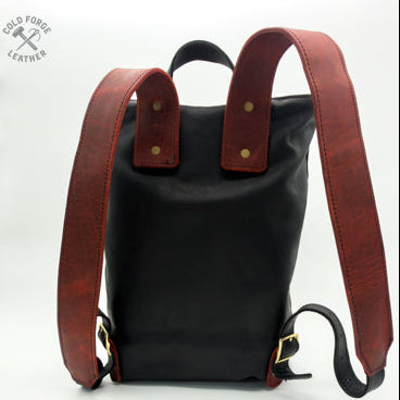 A black leather backpack with contrasting reddish leather shoulder straps and top, shown from the back on a white studio background. 