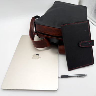 A black leather backpack and notebook cover a, displayed next to a silver laptop, pen, and a white textured background. A 'Cold Forge Leather' logo is visible on the right side.