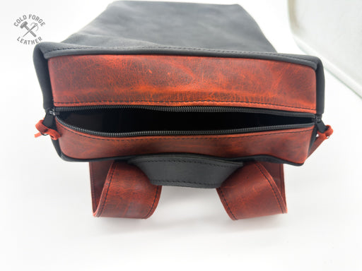 A close-up of a leather bag showing the interior side with a reddishvfront panel, black zipper, black interior lining, and dark gray top flap. 