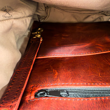 An interior close-up of a redish leather pouch or notebook cover with a zipper, resting inside a beige fabric bag. 