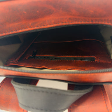 Close-up of the interior of a black leather bag, showing a reddish leather zippered pocket with key clip lanyard and a light beige lining. A