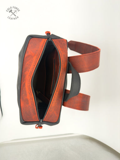 A leather backpack shown open from a side angle, featuring a distressed reddish leather trip with black body and a matching reddish strap, photographed against a plain white background.
