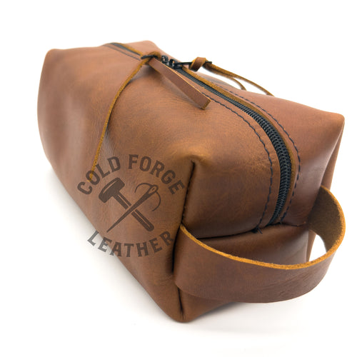 A brown leather zippered pouch with a black zipper and a matching leather strap, shown on a white background. 