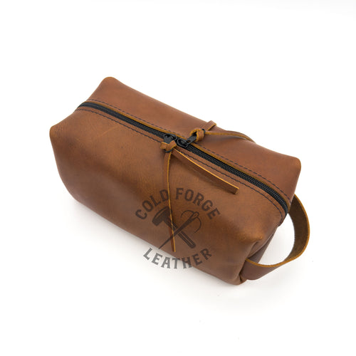 A brown leather zippered pouch with a top handle, shown on a white background. 