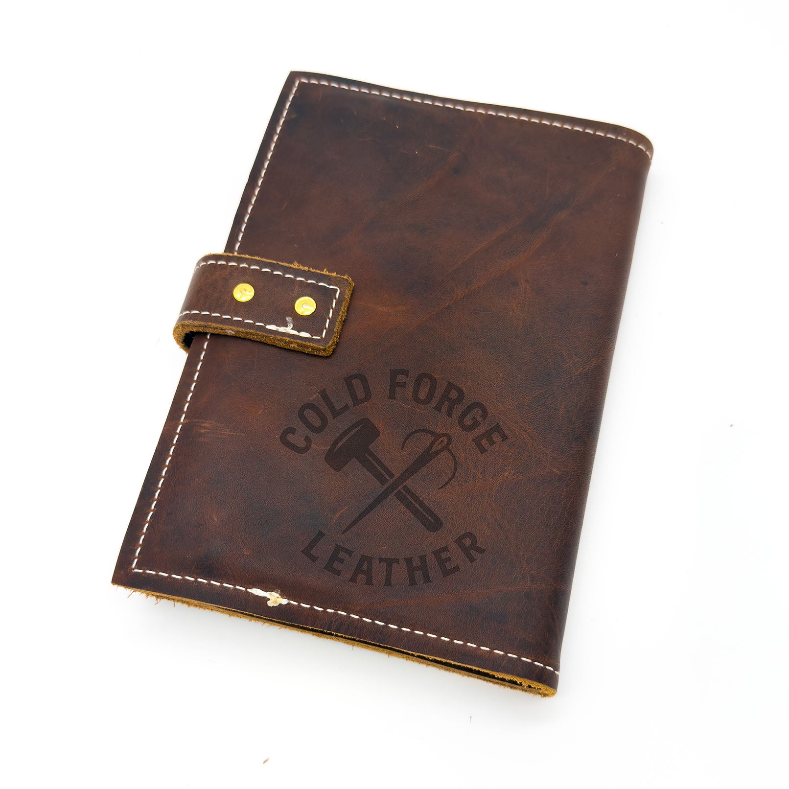 A dark brown distressed leather notebook cover with white contrast stitching, a snap strap closure with brass rivets.