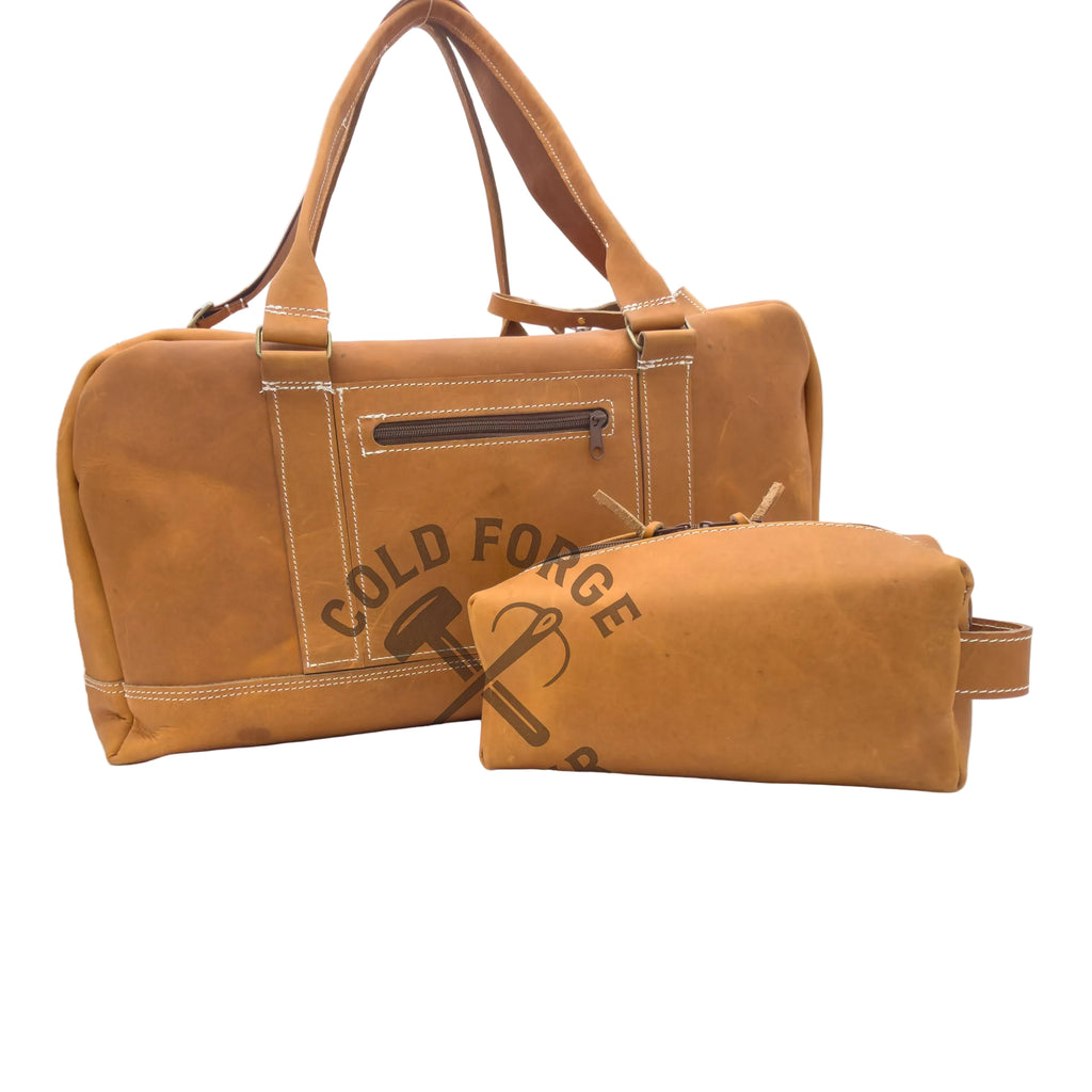 A tan leather duffel bag with dual top handles and a front zip pocket, shown alongside a matching smaller zip pouch. The items are photographed on a white studio surface with a visible 'Cold Forge Leather' watermark across the center.