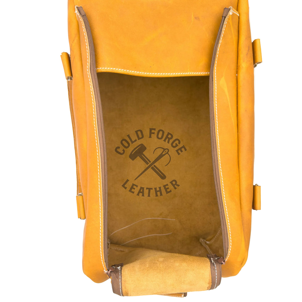 A top-down view of a tan leather bag with its front flap open, showing a tan leather interior printed with the 'COLD FORGE LEATHER' logo. The bag is photographed on a clean white background.