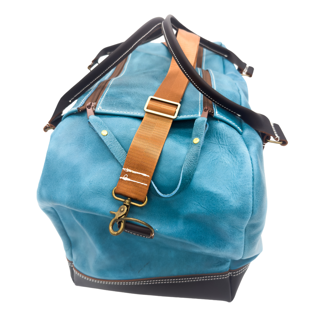 A blue leather duffel bag with black trim, a tan leather strap, and brass hardware, shown on a plain white background.